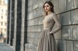 © Larisa - Elegant woman in modest beige dress against urban backdrop
