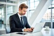 © Manatsavee - Businessman in Black Suit Typing on Laptop at White Table in Modern Office Environment Close Up