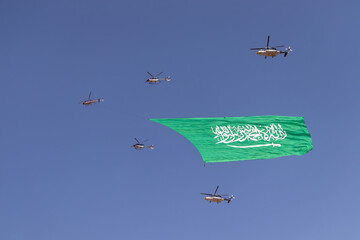 Helicopter carrying the flag flying in the sky, celebrating national occasions and holidays, National Day September 23 anniversary, Banner of monotheism and Islam and the emblem of national identity