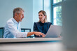 © Westend61 - Smiling senior businessman discussing with colleague over laptop at desk in office