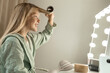 © Westend61 - Happy blond girl curling hair in front of mirror