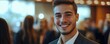 © AIsofeel - A confident young man smiles in a bustling event, radiating positivity and professionalism in a stylish suit.