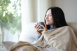 © Antonioguillem - Asian woman in winter drinking coffee covered with blanket at home