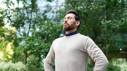 mature male professional standing in city park, eyes closed, taking deep breath. concept of relaxati