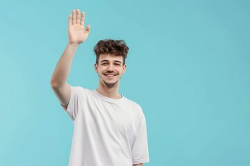 Happy young man with charming expression waves in casual attire on light blue background. Confident and photogenic male model with positive attitude. Cheerful and friendly guy says hello.