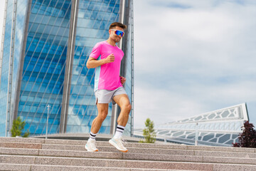 Active Male Runner in Bright Pink Shirt Descends Steps Near Modern Architecture on a Cloudy Day in the City