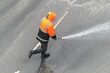 © Semiglass - Man in orange overalls washes road with hose