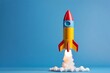 © Adam - Launching rocket toy isolated on blue background with space. A symbol of business growth, startup success, and innovation, representing rising potential, future opportunities, and ambitious ventures.