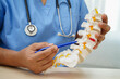 © manassanant - Asian doctor holding spinal nerve and bone model, Lumbar spine displaced herniated disc fragment for treatment medical in the orthopedic department.