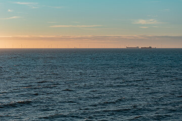 silhouette of the wind farm at the horizon during twilight, two transport vessels on the right. land