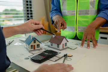 two architect is in office and sharing their strategy idea of building plan to each other, there are blueprint and house model on the desk in the office with two engineers, meeting