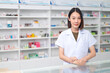 © PhugunStock - Asian professional female pharmacist standing with arms crossed looking at camera charming smile pointing hand to pill bottle health care products in pharmacies Close-up and wide-angle shots