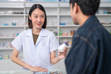 Wall Mural - Asian professional female pharmacist using a digital tablet computer to dispense prescription medication to male customers. The doctor advises and explains to the client about the medication.