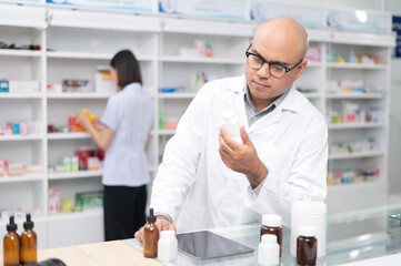 Asian professional male pharmacist using digital tablet computer checking drug list Pharmacist checking stock in pharmacy for health medicine in pharmacy with female pharmacist in the background