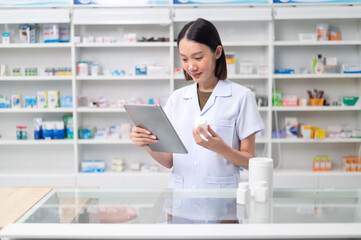 Wall Mural - Asian professional female pharmacist using tablet to check drug list Pharmacist checking stock in pharmacy for health medicine in technology pharmacy looking at camera smiling