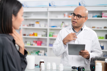 Wall Mural - Asian professional male pharmacist using a tablet to dispense prescription medicines to female customers. The doctor advises and explains to the client how to use the medication.