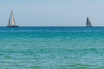 Two sailboats on the horizon sailing in opposite directions on the blue sea