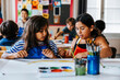 © Maskot - Female students discussing while painting during art class at elementary school