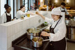 © Maskot - High angle view of female chef multi-tasking while standing with colleagues in commercial kitchen