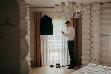 Wall Mural - A man is getting dressed in a room with a white bed and a black jacket hanging on a door