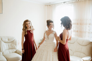 Wall Mural - Three women are getting ready for a wedding. One of them is wearing a white dress. The other two are wearing red dresses. They are standing in front of a white couch