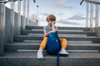 © Cavan Images - Little boy, schoolboy, with a backpack sits on stairs and is sad
