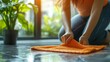 © Kingboy - Person cleaning the floor with a bright orange cloth in the morning