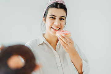 Young caucasian woman eating and posing with donuts on white wall