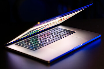 A laptop computer with a half-open screen on a dark background.