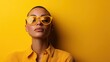 © familymedia - A woman wearing yellow sunglasses blends into a vibrant yellow backdrop, portraying fashion, bold style, and the confident embrace of monochromatic aesthetics.