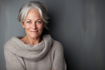 Poster - Portrait of a smiling woman in her 50s dressed in a warm wool sweater while standing against bare monochromatic room