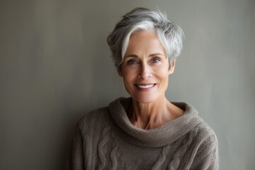 Poster - Portrait of a happy woman in her 60s dressed in a warm wool sweater isolated in bare monochromatic room