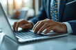 © supattra - Businessman typing on a laptop keyboard at a white office desk, close-up of hands with a tie and suit, working in a modern technology lifestyle concept.