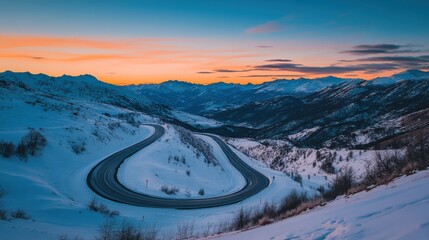 As twilight descends, a winding mountain pass is blanketed in fresh snow, with vibrant hues of orange and blue painting the sky above the serene winter landscape