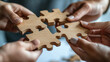 © abdlkerim - The concept of team work and collaboration in business, people's hands holding wooden puzzle pieces together on a white background,