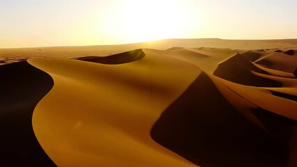 Wall Mural - Sunrise casting warm glow over desert with towering sand dunes