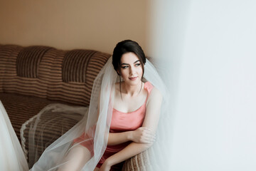 A woman in a white robe is sitting in front of a window, brushing her hair. She is wearing a tiara and a veil, and her hair is styled in a bun. Concept of elegance and sophistication