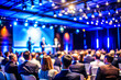 © sanjit536 - Business Conference Speaker Presenting to a Large Audience in a Professional Setting, on dark blue background