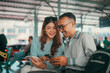 © Odua Images - Two friends joyfully sharing smiles and smartphone moments together at a bustling station