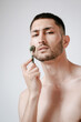 © Elina Leonova - A handsome young man in a wellness center uses a jade guasha roller on his face , highlighting beauty and relaxation in an spa setting
