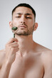 © Elina Leonova - A handsome young man in a wellness center uses a jade guasha roller on his face , highlighting beauty and relaxation in an spa setting