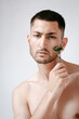 © Elina Leonova - A handsome young man in a wellness center uses a jade guasha roller on his face , highlighting beauty and relaxation in an spa setting