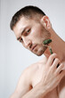 © Elina Leonova - A handsome young man in a wellness center uses a jade guasha roller on his face , highlighting beauty and relaxation in an spa setting