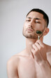© Elina Leonova - A handsome young man in a wellness center uses a jade guasha roller on his face , highlighting beauty and relaxation in an spa setting
