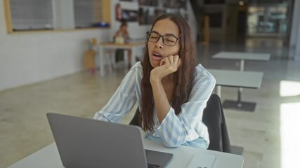 Poster - Woman tired working on laptop in office wearing glasses and striped shirt, showcasing a modern workplace setting with an open interior design.