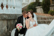 © Vasil - A bride and groom are sitting on a bench, the bride holding a bouquet of flowers. Scene is romantic and intimate