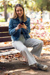 © nenetus - Pretty young woman using her mobile phone while sitting on a bench in the park.