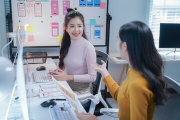 Two asian ui/ux designers discussing a new mobile app in a modern office. Focused on work. They showcase expertise in web and app development. Reflecting teamwork and creativity in a startup setting