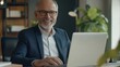 © Johannes - Smiling mature adult business man executive sitting at desk using laptop. Happy busy professional mid aged businessman ceo manager working on computer corporate technology in office