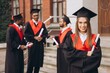 © anatoliycherkas - Joyful Young Woman Celebrating Graduation with Friends in Academic Gowns Outdoors